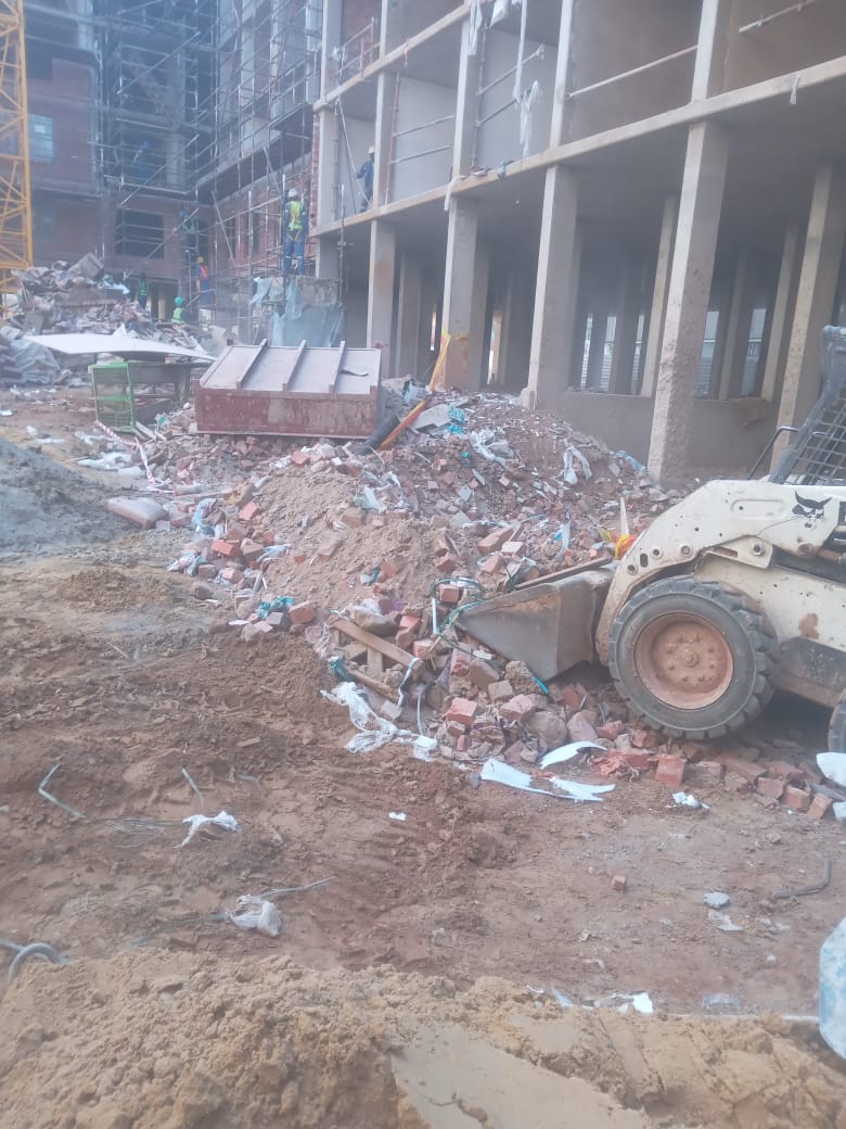 Skid-steer loader clearing rubble at a scaffolded building